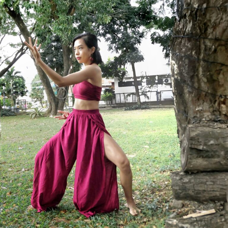 A woman in all red outfit practicing qigong outside in the park