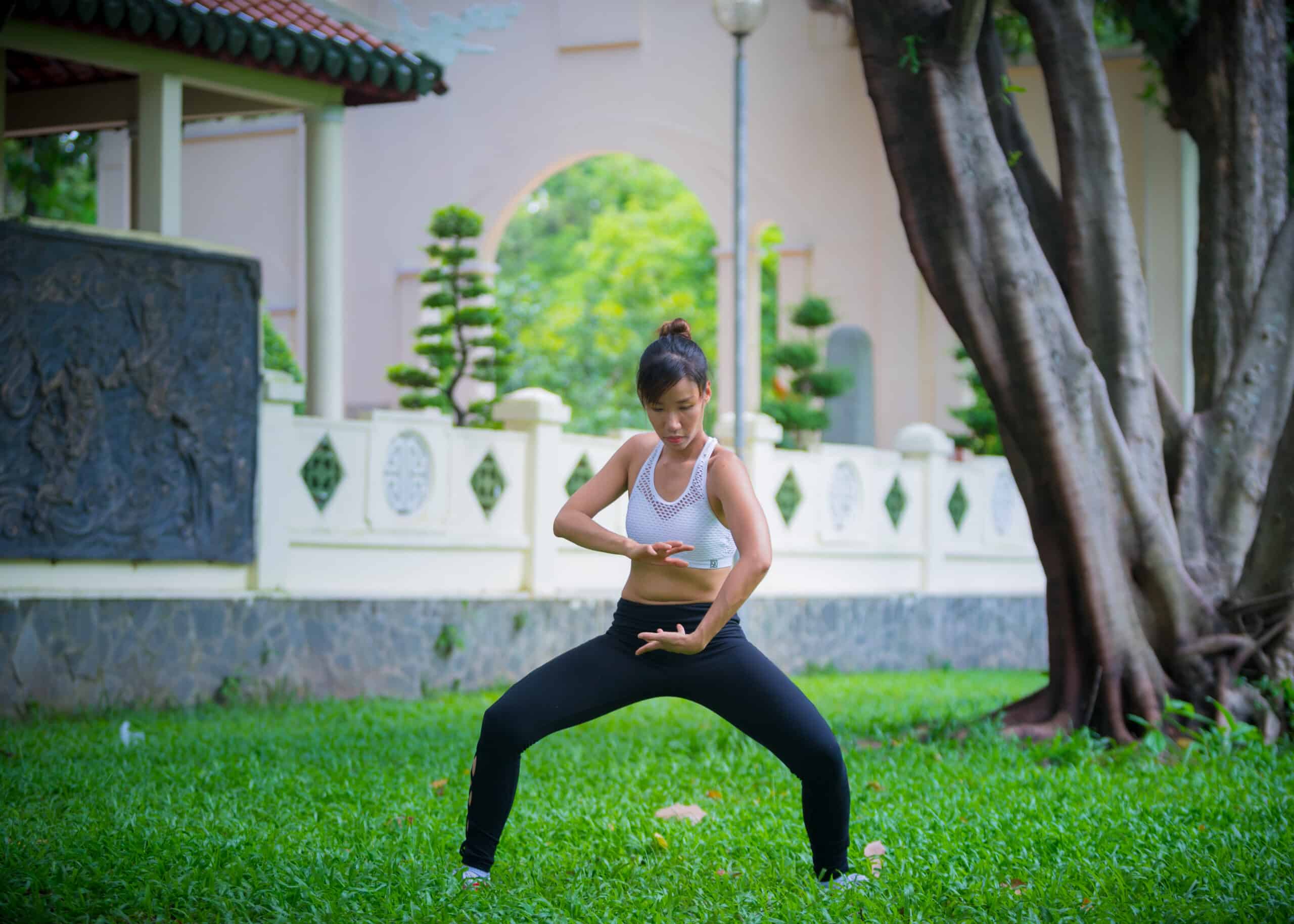 Qigong for hip pain - A woman wearing black and white sporty outfit practicing dragon ball qigong outside surrounded by nature 